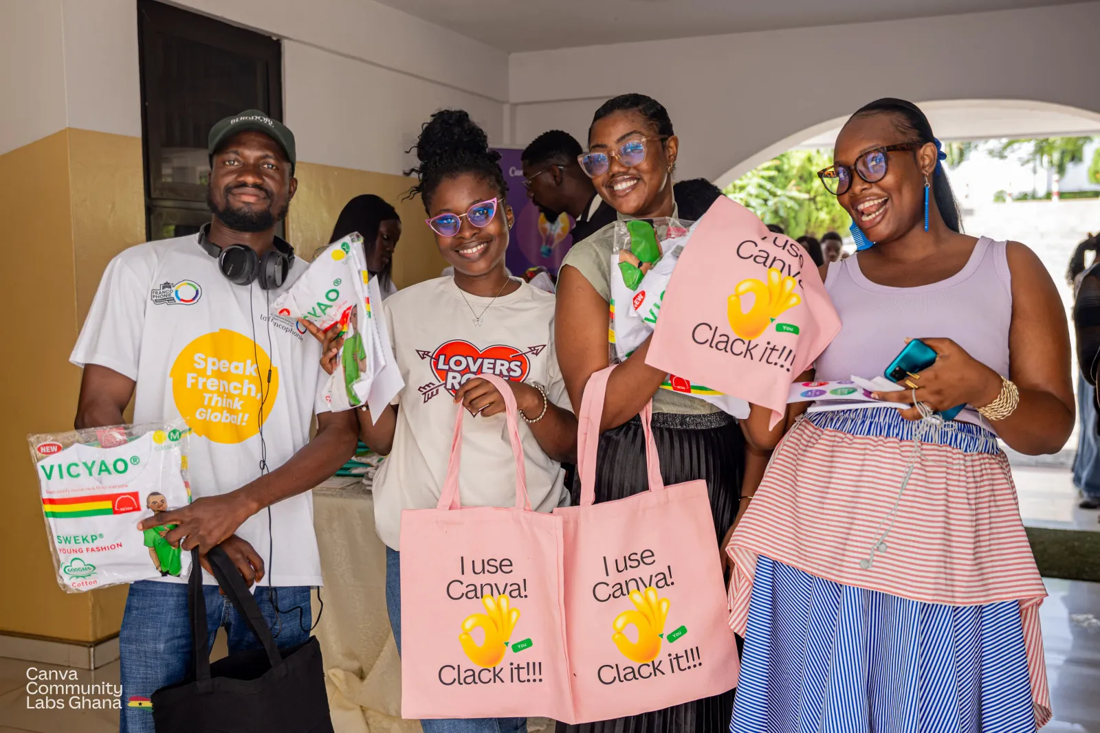 Four attendees in a corridor holding up pink tote bags printed with the words I use Canva, clack it.